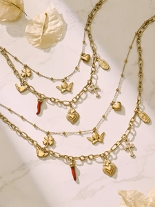Detailed top view of layered gold necklaces with heart, cross and red chili charms