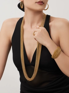 Detail van 18k vergulde gelaagde kettingen en brede wikkelarmband gedragen door model