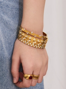 Detail of layered gold bangles with teardrop zircons and clover charms on model