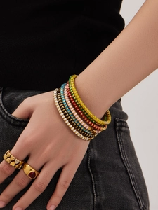 Detailansicht bunter Emaille-Armbänder und goldener Herzringe an einem Model