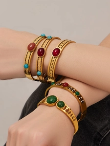 Dettaglio di bracciali geometrici dorati impilati con pietre rosse e verdi incastonate