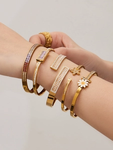 Detalle de pulseras doradas superpuestas con circonitas de colores y margarita