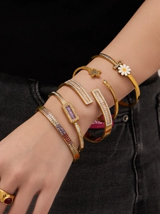 Detalle de brazaletes dorados en capas con motivos de margaritas y dijes de circón