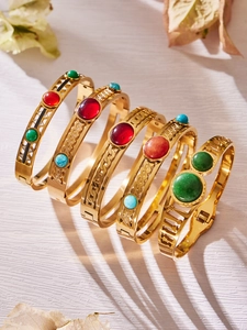 Dettaglio di 5 bracciali geometrici dorati con pietre colorate su sfondo di legno