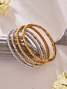 Nahaufnahme von gestapelten Armreifen aus Gold und Silber auf minimalistischem Stein