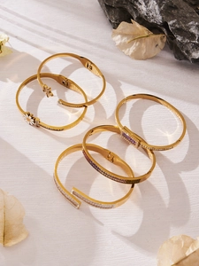 Detalle de pulseras doradas con margaritas de circón y piedras púrpuras en textura