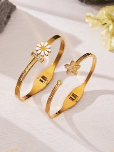 Detalle de brazaletes dorados con margaritas y circonitas sobre fondo de madera blanca