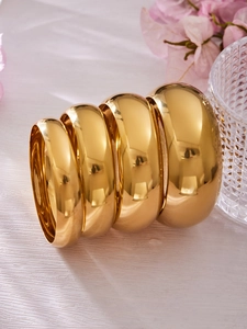 Primer plano de cuatro brazaletes minimalistas de acero inoxidable pulido espejo de oro 18k