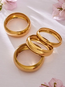 Primer plano de cuatro brazaletes apilados de acero inoxidable bañados en oro de 18k