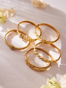 Detail of five 18k gold plated stainless steel bangles with zircon inlays on wood