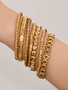 Detailed close-up of 7-piece stacked gold bangles featuring heart motifs and textured metal