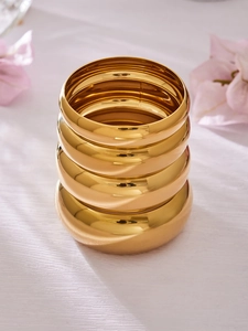 Primer plano de cuatro brazaletes apilados de acero inoxidable pulido bañados en oro 18k