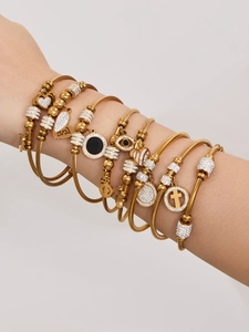 Detail von goldenen Stapelarmbändern mit Auge, Herz und Kreuz Anhängern am Handgelenk