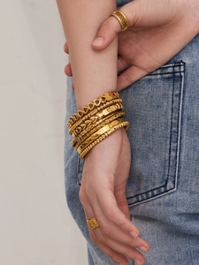 Dettaglio di bracciali e anelli dorati a strati con trame a cuore e geometriche