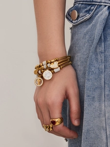 Details goldener mehrlagiger Armbänder mit Kreuzanhängern und roten Herz-Edelsteinringen
