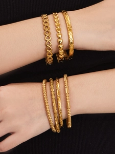 Dettaglio di bracciali in acciaio dorato 18k con cuore e design geometrico trapuntato