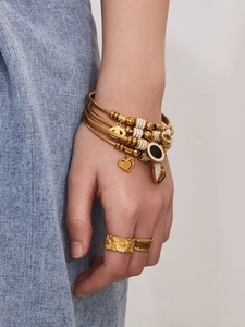 Detail von mehrlagigen Goldarmbändern mit Zirkonia-Anhängern und Logo-Charms am Handgelenk