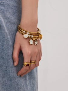 Dettaglio del bracciale dorato con ciondoli e anello con rubino a cuore sulla mano