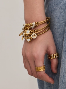 Dettaglio di bracciali a cavo dorati con ciondoli a stella e cuore sul polso