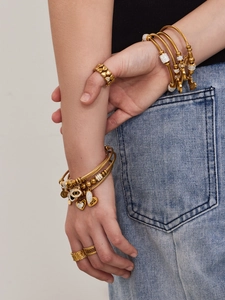 Nahaufnahme gestapelter goldener Kabelarmbänder mit Herz- und Augenanhängern am Handgelenk