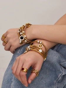 Detailansicht von goldenen Armbändern mit Kreuz- und Herzanhängern am Handgelenk