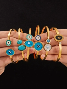 Détail de bracelets ouverts œil protecteur en or avec turquoise sur fond noir uni