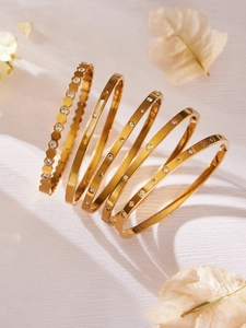 Sechs goldene Edelstahlarmbänder mit Zirkon-Inlay auf strukturiertem weißem Hintergrund