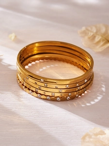 Detailaufnahme von fünfteiligem Goldarmband-Set mit Zirkon-Akzenten auf Holz