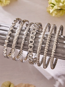 Dettaglio di sette bracciali in acciaio argento con motivi a cuore e a treccia