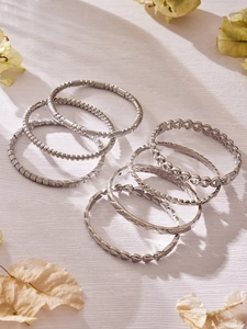 Dettaglio del set di bracciali argentati testurizzati su sfondo di legno naturale