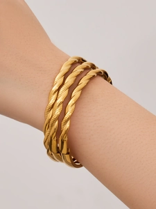 Primer plano de tres brazaletes de cuerda trenzada chapados en oro de 18k con acabado pulido