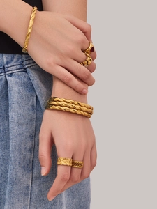Primer plano de un set de joyas doradas con brazaletes trenzados y anillos de estilo lujo
