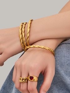 Detalle de brazalete dorado multicapa trenzado y anillo de corazón rojo en la muñeca