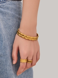 Detalle de brazalete trenzado bañado en oro de 18k y anillos en modelo con ropa vaquera