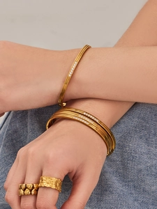 Stacked 316L gold bangles with 5A cubic zirconia stones worn over denim fabric