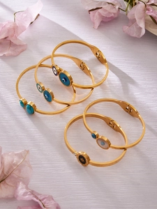 Détail de bracelets dorés avec œil protecteur et turquoise sur fond de fleurs roses