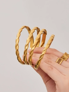 Primer plano de brazaletes trenzados bañados en oro 18k y anillo de girasol elegante
