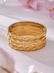 Juego de cuatro brazaletes de acero inoxidable bañados en oro de 18K en madera blanca