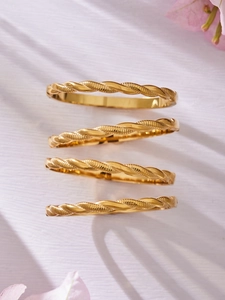 Detalle de cuatro brazaletes retorcidos de acero inoxidable chapados en oro de 18k