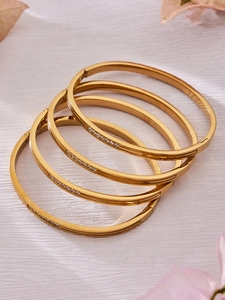 Detail of four stacked gold-plated bangles with geometric grooves and 5A zircon stones