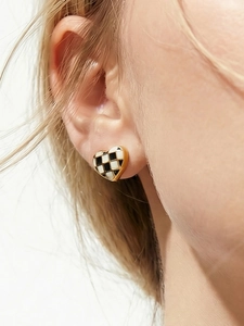 Gros plan d'une boucle d'oreille cœur avec émail à damier noir et blanc et bord doré