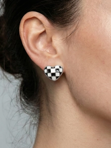 Gros plan d'une boucle d'oreille cœur à damier en émail portée par une femme modèle