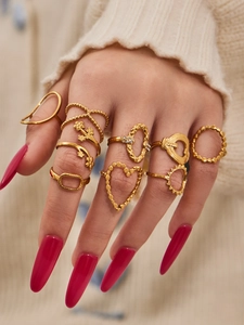 Detail of gold geometric heart rings set on fingers with pink nails and white sweater