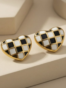 Détail de boucles d'oreilles cœur avec motif en émail à damier noir et blanc