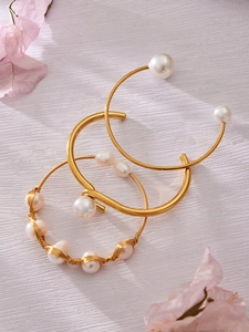 Detalle de brazaletes dorados con perlas sobre fondo texturizado con pétalos rosas