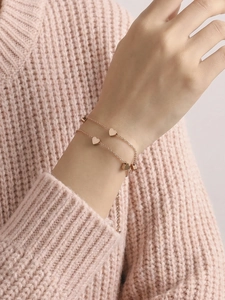 Detail of rose gold double-layered bracelet with heart pendant on soft pink knit
