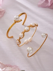 Detalle de tres brazaletes bañados en oro de 18k con perlas naturales sobre fondo de pétalos