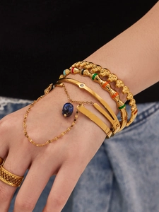 Gros plan de bracelets dorés superposés avec émail, breloque en pierre et bague dorée