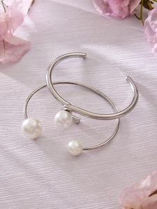 Detalle de brazaletes abiertos plateados con perlas de agua dulce y detalles florales rosas