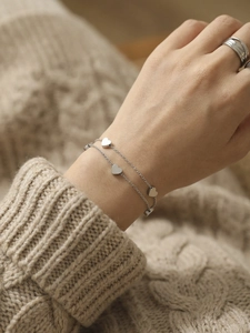 Close-up of double-layer stainless steel heart charm bracelet worn on a sweater sleeve